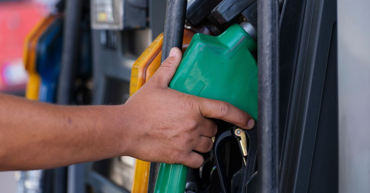 Close-up of a hand holding a green fuel nozzle at a gas pump station outdoors.